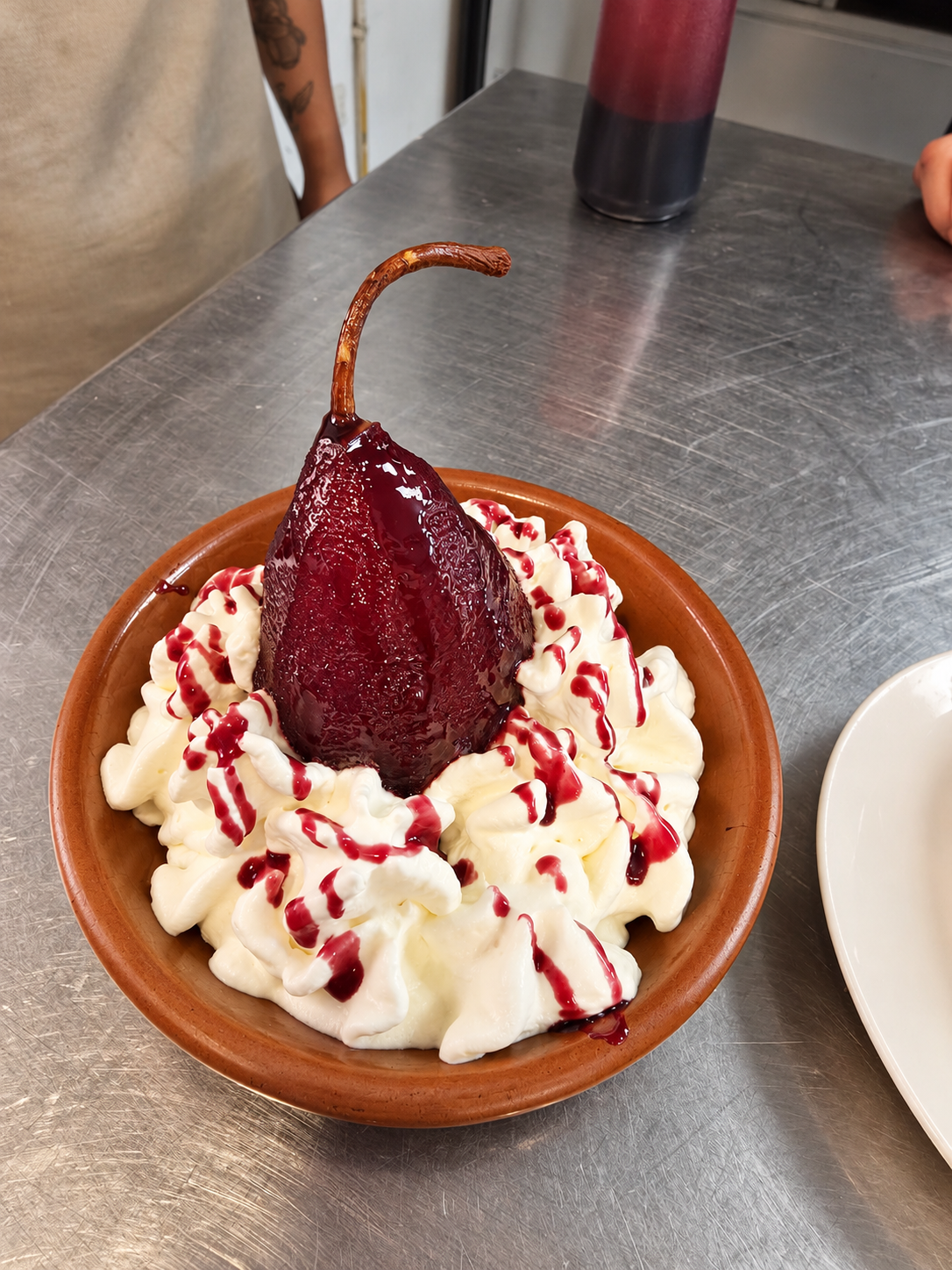 Pera al vino con crema servida en un plato de cerámica.
